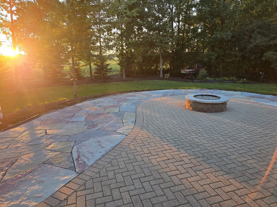 A circular fire pit on a curved paver patio with colorful natural stone edging at sunset