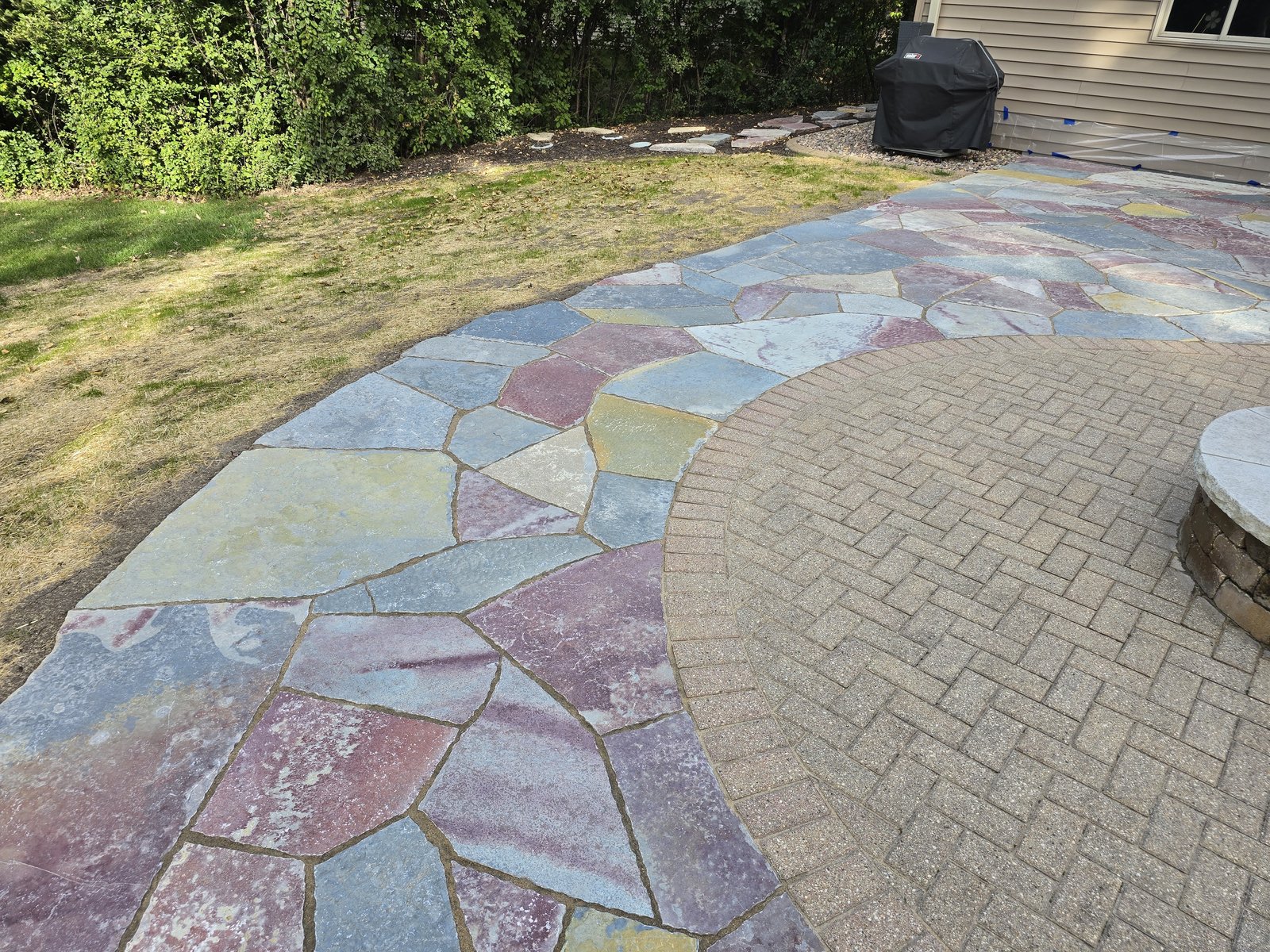 Close view of multicolored flagstone meeting a curved herringbone paver patio