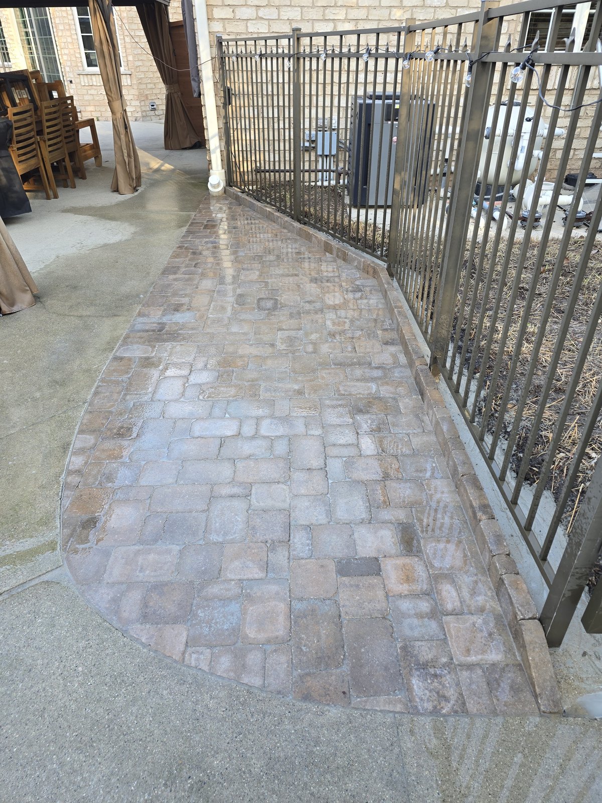 A fitted paver path between an existing concrete patio and a black metal fence