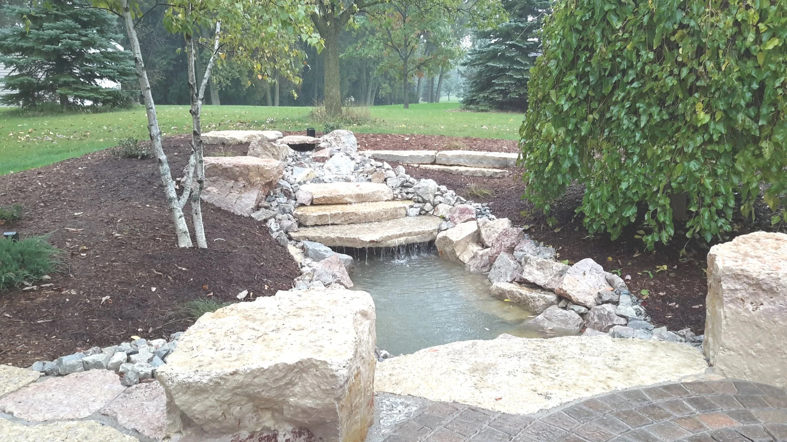 A garden water feature with cascading natural stone ledges and lush surroundings
