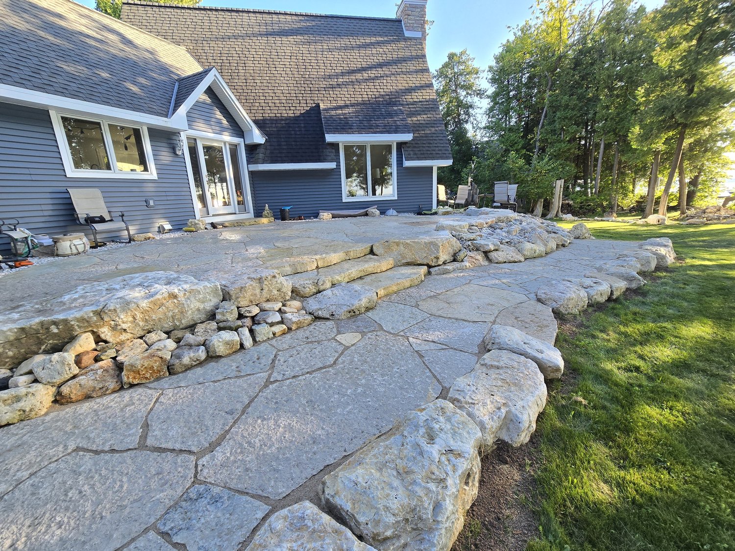 Tiered natural stone patio with broad stone steps and boulder edging beside a home