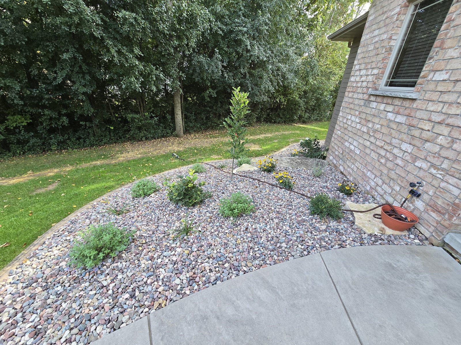 A curved river rock garden bed with small shrubs and flowering plants beside a patio